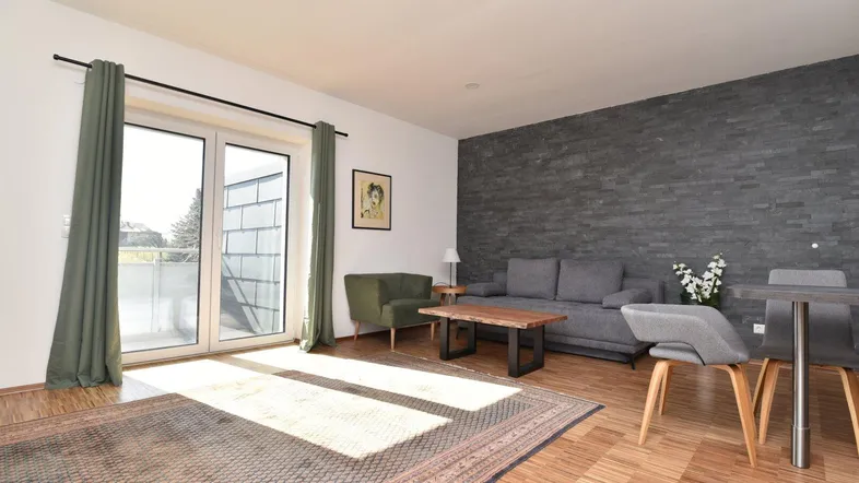 Helles Wohn- und Esszimmer mit Holzboden, dekorativer Steinwand und Zugang zum Balkon.