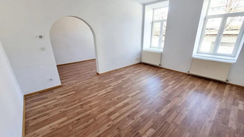 Helles Wohnzimmer mit Laminatboden und zwei Fenstern, bereit zur individuellen Gestaltung.