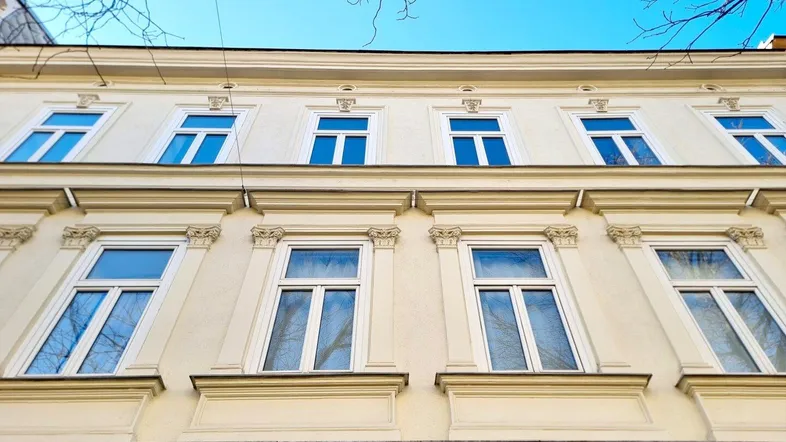 Fassade eines Altbaus mit mehreren Fenstern und dekorativen Elementen unter blauem Himmel.