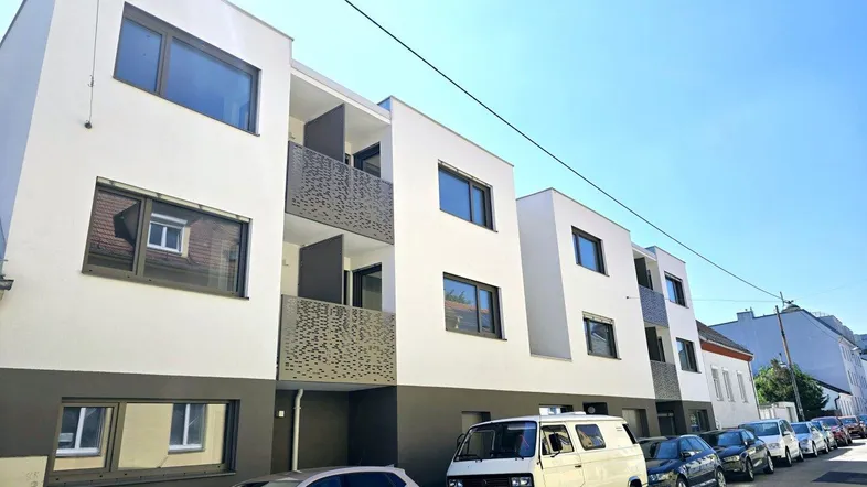 Moderne Wohnanlage mit weißer und grauer Fassade, Balkonen und parkenden Autos auf der Straße.