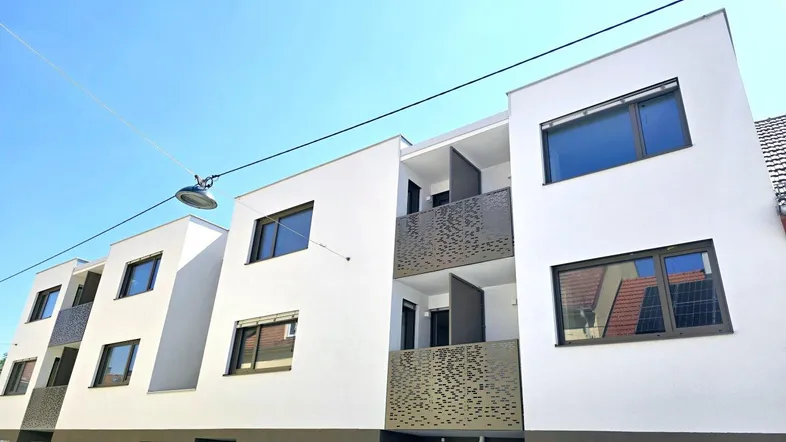 Moderne Wohnanlage mit weißer Fassade, Balkonen und großen Fenstern an einem sonnigen Tag.