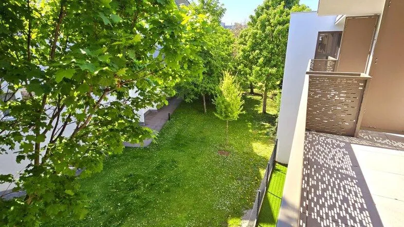 Heller Balkon mit Blick auf den grünen Garten und die umliegenden Bäume an einem sonnigen Tag.