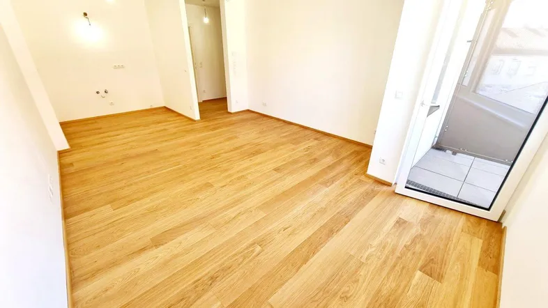 Helles Zimmer mit neuem Holzparkettboden und Zugang zu einem Außenbereich.