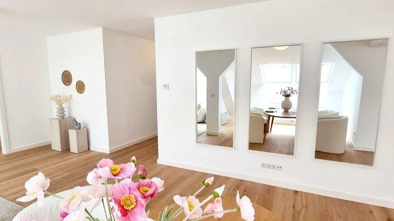 Heller Wohnbereich mit Holztisch, Blumen und dekorativen Spiegeln, die den Raum optisch vergrößern.