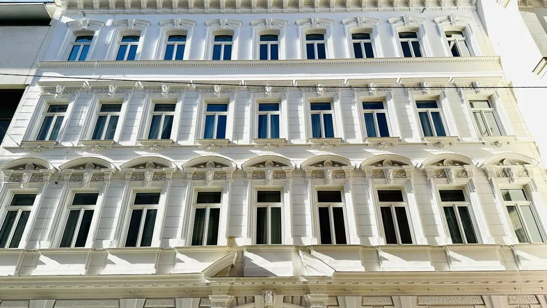 Eindrucksvolle weiße Fassade eines historischen Gebäudes mit vielen Fenstern und dekorativen Elementen.