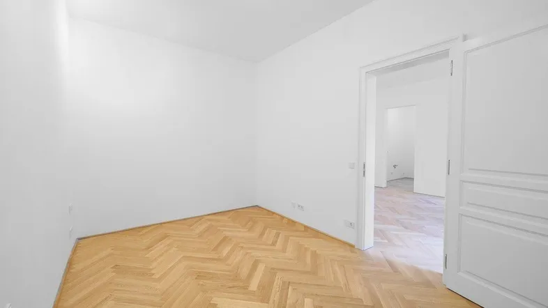 Heller Raum mit Fischgrätparkettboden und weißen Wänden, bereit für individuelle Gestaltung.
