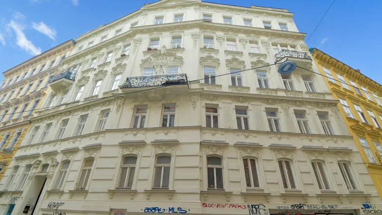Historisches Gebäude mit reich verzierter Fassade, mehreren Stockwerken und Balkonen unter blauem Himmel.