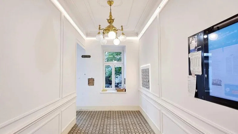 Eleganter Flur mit gemustertem Fliesenboden, Stuckdecke und klassischer Beleuchtung, hell und einladend.