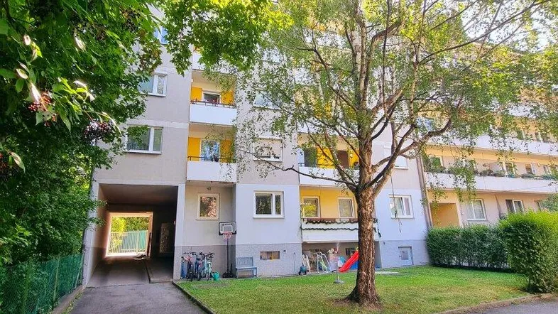 Mehrfamilienhaus mit grüner Umgebung, Bäumen und Zugang zum Innenhof.