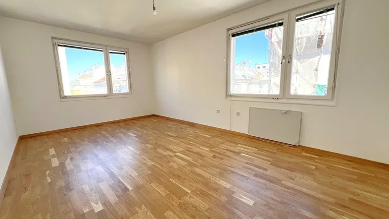 Helles Zimmer mit Parkettboden und zwei großen Fenstern, ideal als Wohn- oder Schlafbereich.