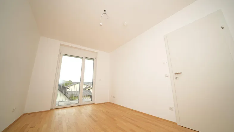 Helles Zimmer mit Holzboden und Zugang zu einem Balkon, ideal als Wohn- oder Schlafbereich.
