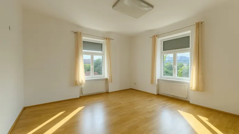 Heller Raum mit Parkettboden und zwei Fenstern, die viel Tageslicht hereinlassen.