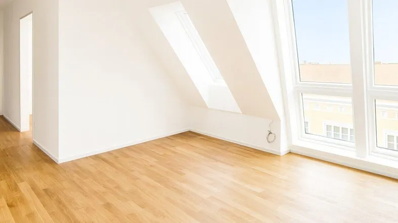 Helles Zimmer mit Dachschrägen, großen Fenstern und hellem Parkettboden.