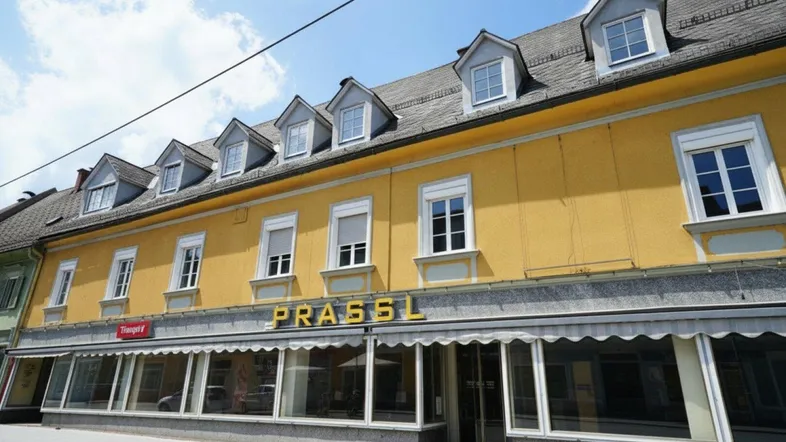 Historisches Gebäude mit gelber Fassade, vielen Fenstern und einem Geschäft im Erdgeschoss an einer Straße.