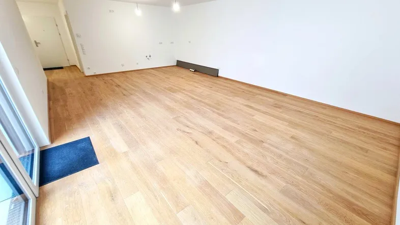 Helles, leeres Zimmer mit neuem Holzparkettboden und weiß gestrichenen Wänden, bereit zur Einrichtung.