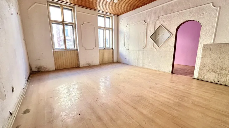 Geräumiges Zimmer mit Holzbalkendecke und Parkettboden, das deutlichen Renovierungsbedarf aufweist.