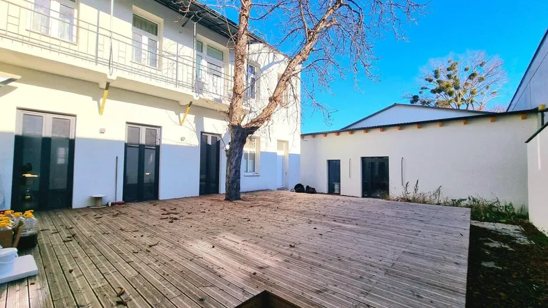 Geräumige Holzterrasse im Innenhof mit einem Baum und Zugang zu mehreren Gebäudeeingängen.