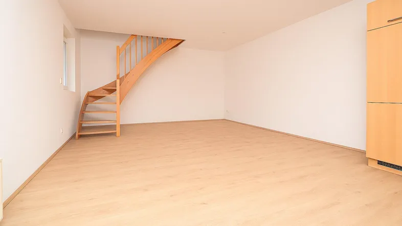 Leerer Raum mit Holztreppe, Laminatboden und viel natürlichem Licht.
