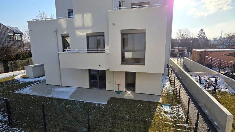 Modernes Mehrfamilienhaus mit weißer Fassade und umliegender Grünfläche im Winter bei Sonnenschein.