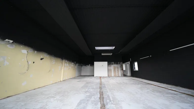 Weitläufiger Gewerberaum mit schwarzer Decke und Wänden, hellem Betonboden und Oberlicht für Tageslicht.