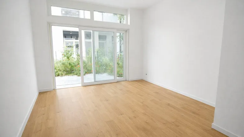 Helles, leeres Zimmer mit großen Schiebetüren und Zugang zu einem kleinen Außenbereich.