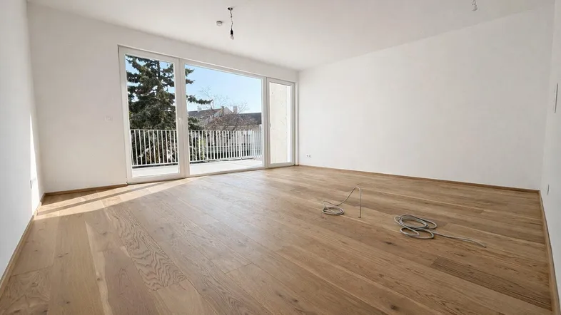 Heller Wohnraum mit neuem Holzparkettboden und großem Fenster mit Balkonzugang.