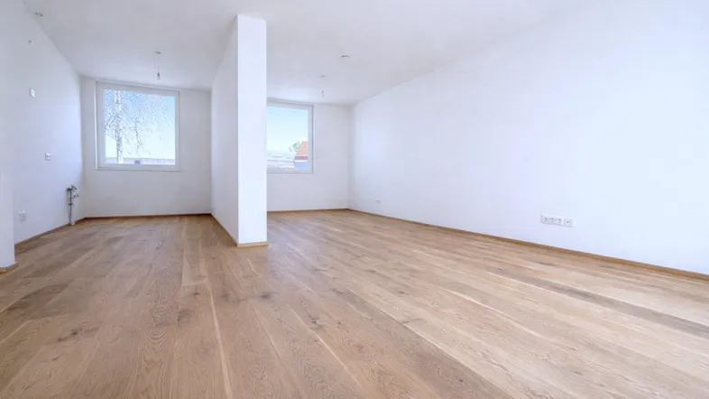 Helles, leeres Zimmer mit neuem Holzboden und großen Fenstern, bereit zur Einrichtung.