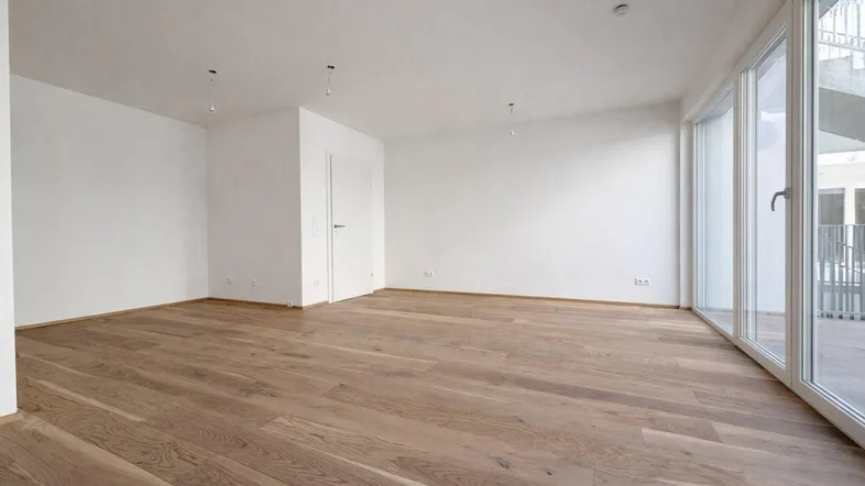 Helles, leeres Zimmer mit modernem Parkettboden und großen Fenstern, bereit zur individuellen Gestaltung.
