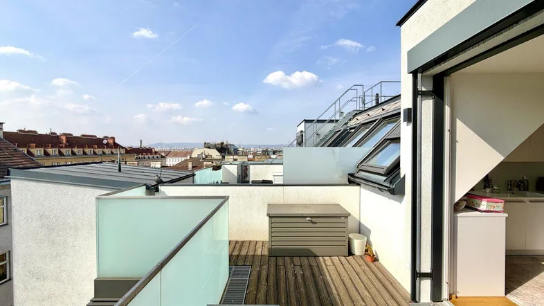 Geräumige Dachterrasse mit Holzboden, Glasgeländer und weitem Blick über die Stadt.