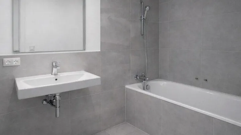 Modernes Badezimmer mit grauen Fliesen, Badewanne und einem schwebenden Waschbecken.