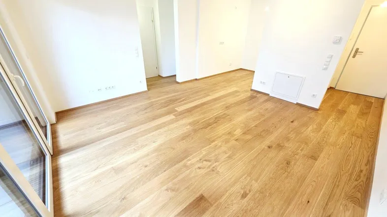 Heller Wohnraum mit neuem Parkettboden und Zugang zu einem Balkon.