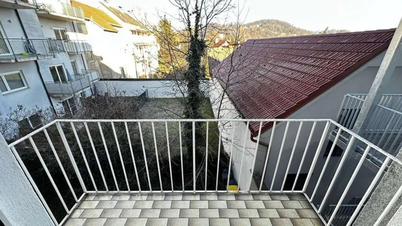 Balkon mit Fliesenboden und Blick auf umliegende Gebäude und Bäume.