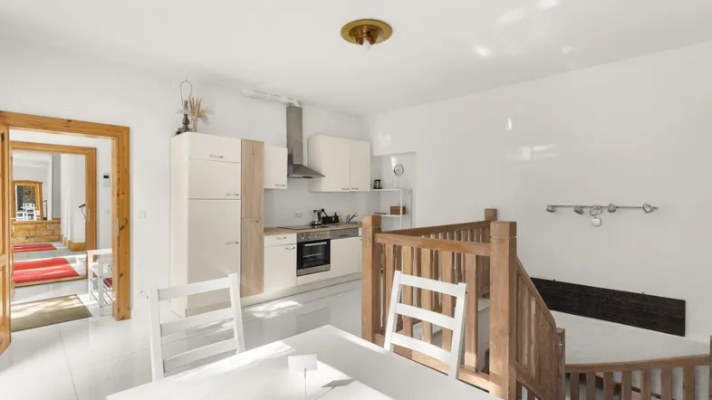Helle, offene Küche mit modernen Schränken, Essbereich und Zugang zu einer Holztreppe.