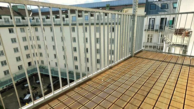 Sonniger Balkon mit Holzboden und Blick auf den begrünten Innenhof.