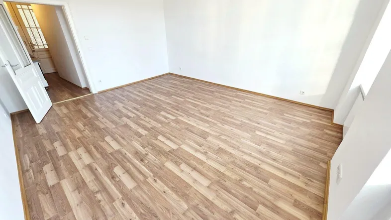 Helles, leeres Zimmer mit Laminatboden und weiß gestrichenen Wänden, bereit zur individuellen Gestaltung.