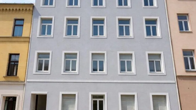 Modernes Mehrfamilienhaus mit heller Fassade und vielen Fenstern unter blauem Himmel.