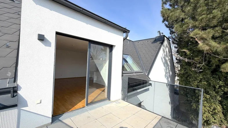 Heller Balkon mit Glasgeländer und Blick auf die umliegende Bebauung und Bäume.