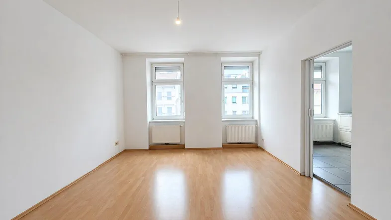 Helles Zimmer mit Laminatboden, weißen Wänden und zwei Fenstern, die viel Tageslicht hereinlassen.