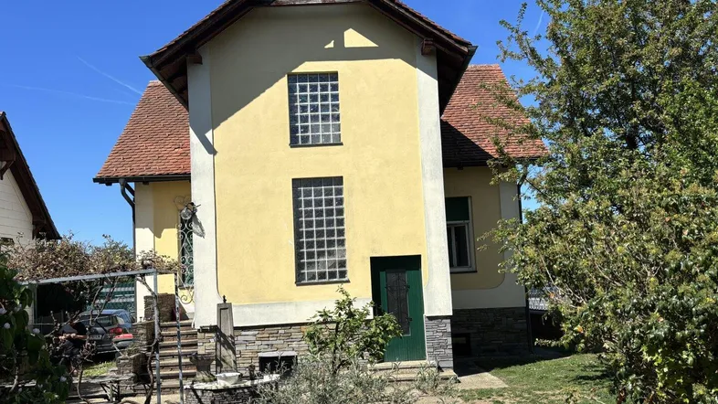 Gelbes Einfamilienhaus mit rotem Ziegeldach und kleinen Fenstern im Grünen.