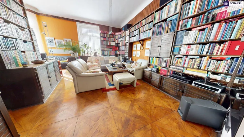 Geräumiges Wohnzimmer mit umfangreichen Bücherregalen, Parkettboden und gemütlicher Sitzecke.