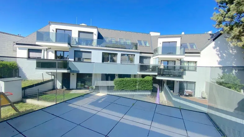 Moderne Wohnanlage mit mehreren Balkonen und Terrassen, umgeben von Grünflächen unter blauem Himmel.