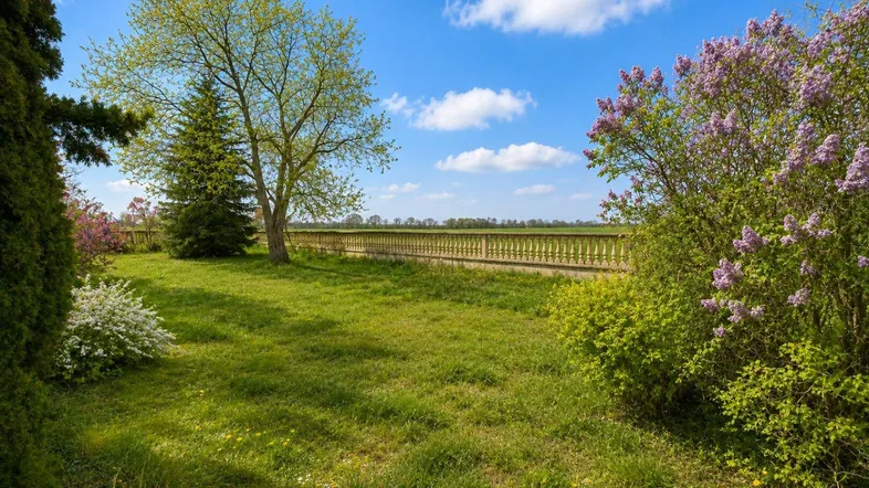 Gepflegter Garten mit blühenden Büschen, Bäumen und einer dekorativen Steinbalustrade.