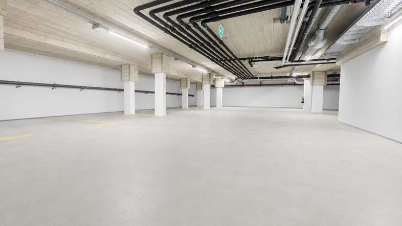 Geräumige Tiefgarage mit Betonboden, freiliegenden Rohren und Säulen, bereit zur Nutzung.