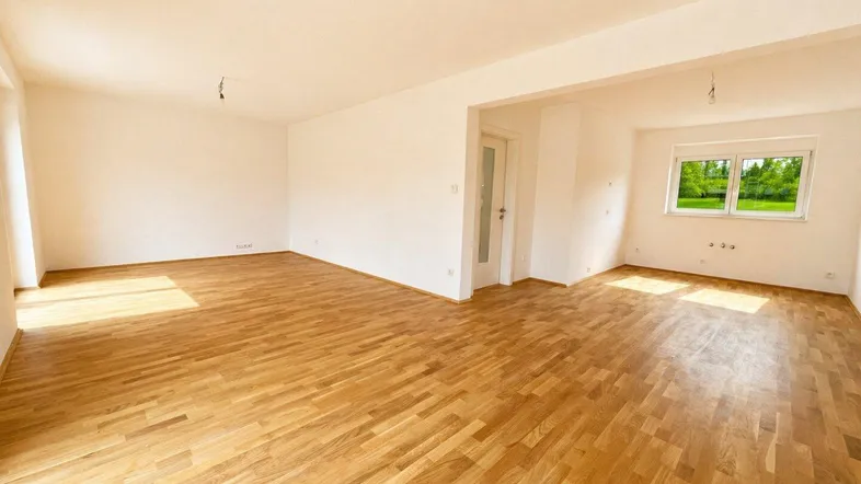 Helles, geräumiges Wohnzimmer mit Parkettboden und Blick ins Grüne durch das Fenster.
