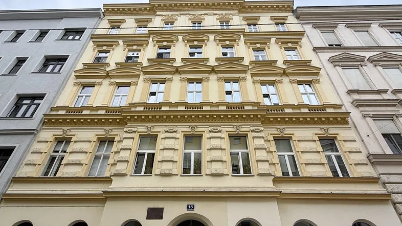 Historische Fassade eines Mehrfamilienhauses mit vielen Fenstern und klassischer Architektur.