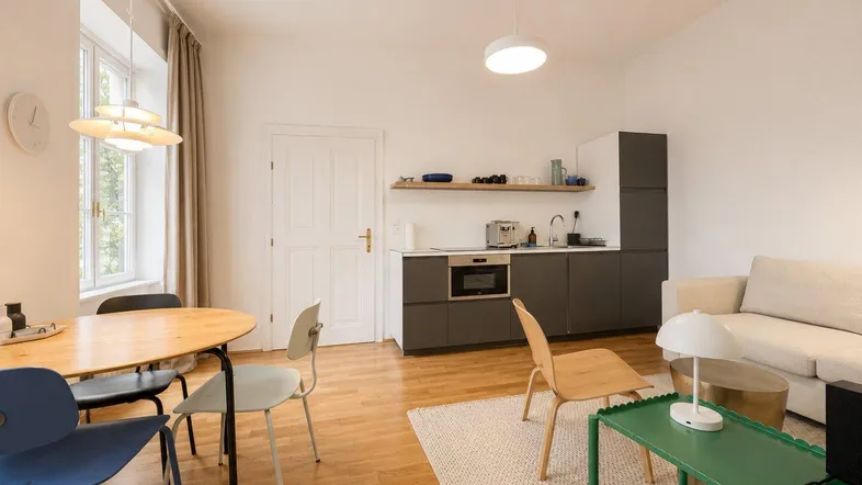 Helles, offenes Wohnzimmer mit integrierter Küchenzeile, Esstisch und Parkettboden.