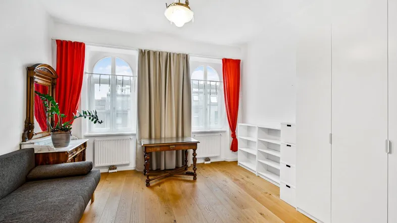 Großes Wohnzimmer mit Holzboden, Sofa, Schränken und zwei hohen Fenstern.