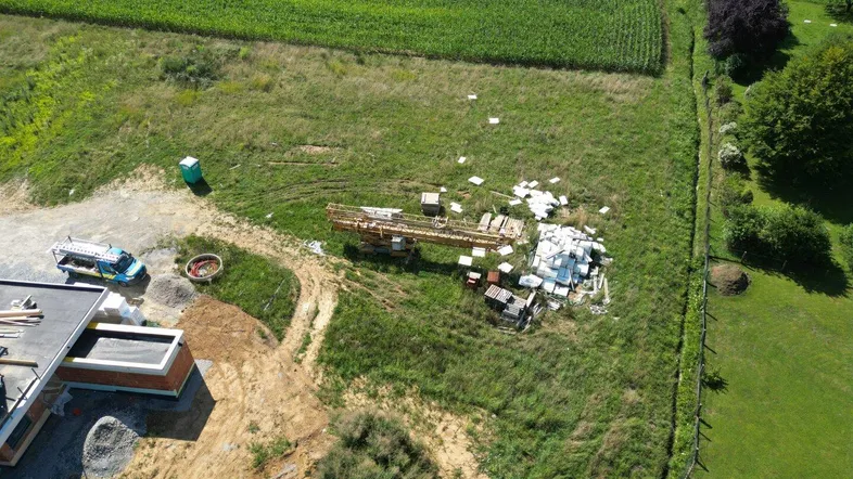 Detaillierte Luftaufnahme einer Baustelle mit Baumaterialien, einem Kran und einem im Bau befindlichen Gebäude.