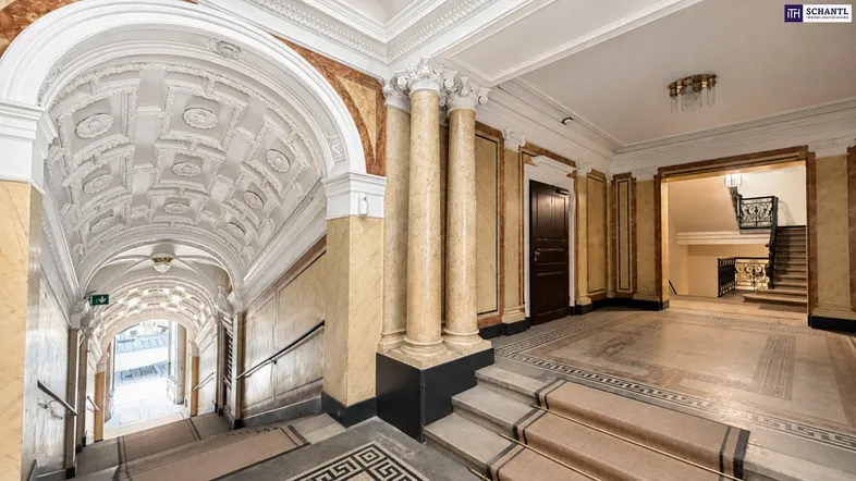 Prunkvolle Eingangshalle mit Säulen, aufwendiger Decke und breiter Treppe, die den historischen Charme bewahrt.