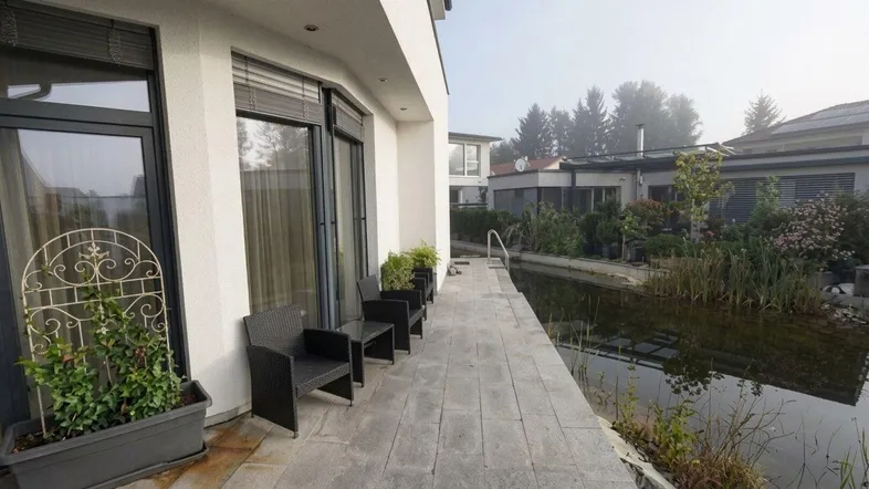 Moderne Terrasse mit Sitzgelegenheiten am Teich, umgeben von grüner Bepflanzung.
